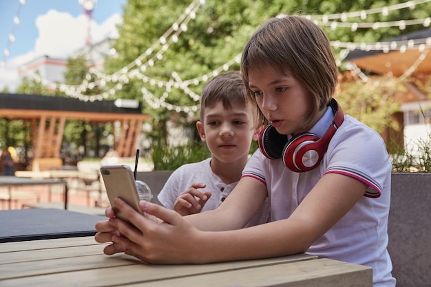 Escolares caucásicos sentados a la mesa en el café veranda usando teléfono móvil