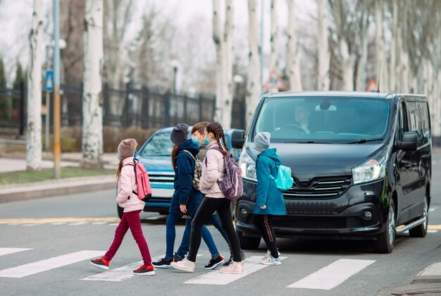 Los escolares cruzan la calle con máscaras médicas. Los niños van a la escuela.