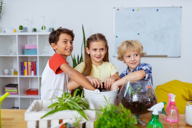 Escolares emocionados. Escolares radiantes y emocionados macetando cactus y plantas juntos en la lección de ecología