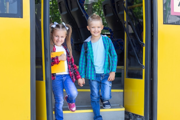 Los escolares felices con mochilas bajan del autobús escolar.