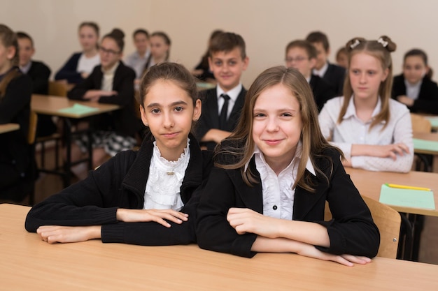 Los escolares felices se sientan en un escritorio en el aula