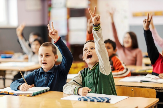 Escolares levantando la mano y respondiendo preguntas en la escuela