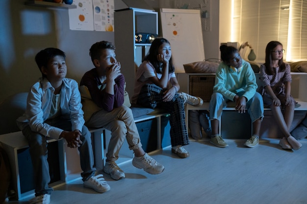 Escolares multirraciales sentados en el aula oscura y viendo una presentación de video