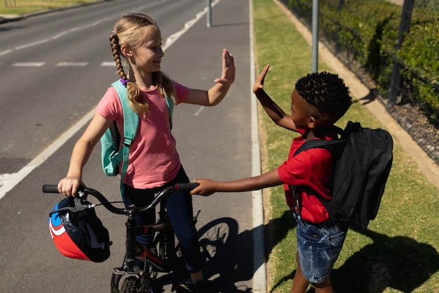 Foto escolares parados en la acera, sosteniendo una bicicleta y chocando los cinco