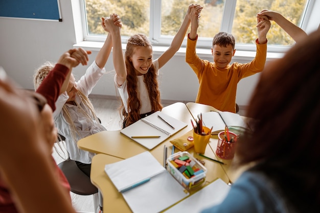 Foto los escolares sentados a la mesa y levantando las manos