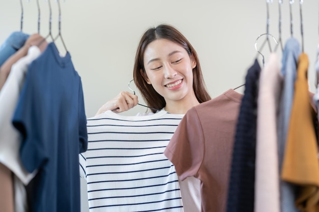 Escolha de roupasNada para vestir Garota jovem asiática atraente experimente aparecer feliz escolhendo roupa de vestido no cabide no guarda-roupa no armário do quarto em casa Decidindo blusa o que colocar em qual