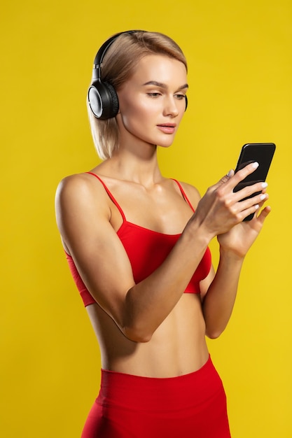 Escolhendo música para uma linda mulher esportiva com fones de ouvido, olhando para o smartphone em pé