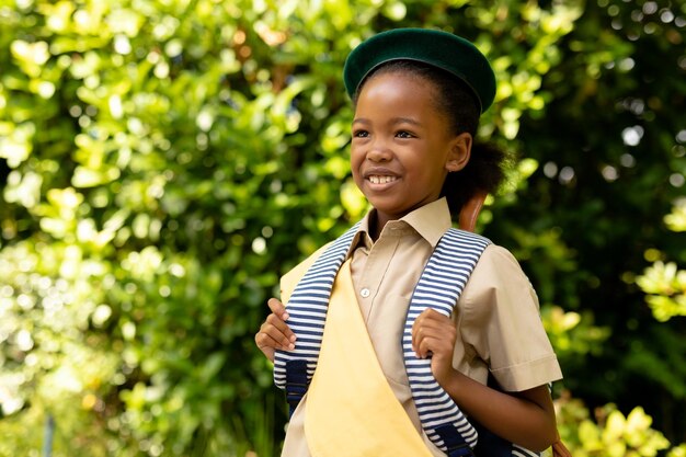 Foto escoteira afro-americana sorridente de uniforme com mochila olhando para as plantas. inalterada, escoteira, infância, coragem, liderança e escotismo.
