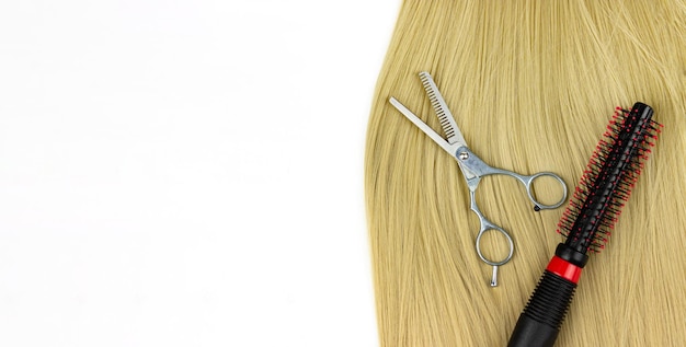 Escova de cabelo redonda de cabeleireiro profissional e tesoura com fio de cabelo loiro em um fundo branco Equipamentos e ferramentas profissionais de cabeleireiro da série