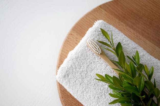 Escova de dentes de bambu amigável de eco na toalha branca e folha verde na tábua redonda de madeira