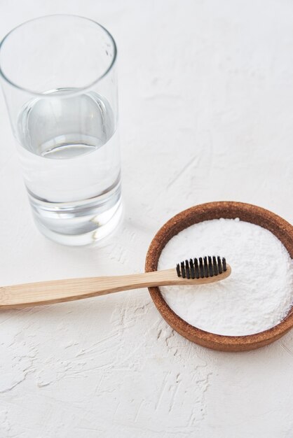 Escova de dentes de bambu, bicarbonato de sódio e copo de água em um fundo branco. escovas de dentes ecológicas, conceito de desperdício zero