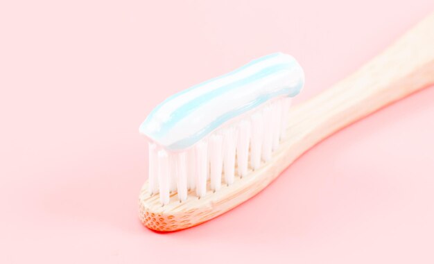 Escova de dentes de bambu com creme dental à direita em um rosa suave