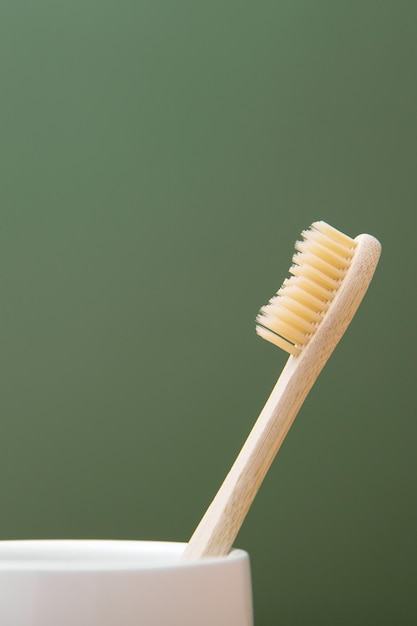 Escova de dentes de bambu de madeira em um copo branco sobre um fundo verde O conceito de sustentabilidade e a rejeição do plástico O conceito de higiene e rotina diária Copy spase foto vertical