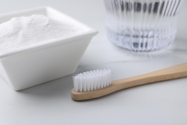 Escova de dentes de bambu e tigela de bicarbonato de sódio na mesa branca fechada