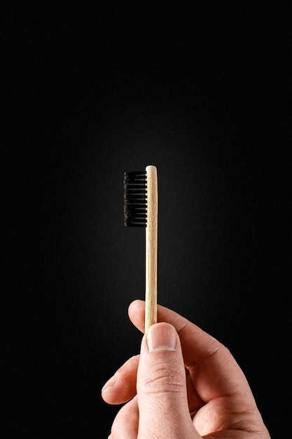 Escova de dentes de bambu ecológica na mão de uma mulher contra um fundo escuro