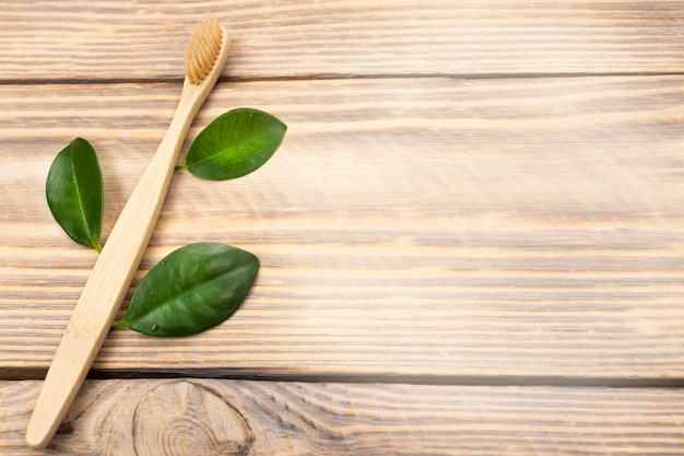 Escova de dentes de bambu ecológica natural com folhas verdes de árvore em uma superfície de madeira