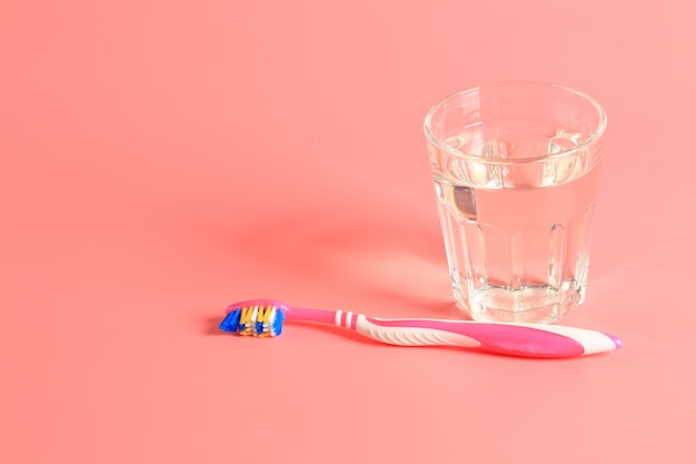 Escova de dentes e um copo d'água em um fundo rosa