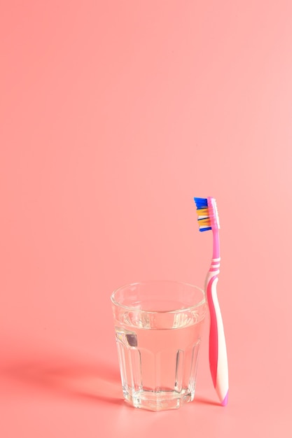 Foto escova de dentes e um copo d'água em um fundo rosa