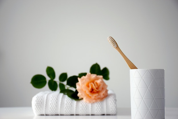 Escova de dentes ecológica de madeira em suporte branco com rosa laranja e toalha branca