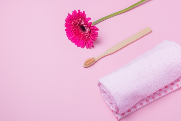 Escova de dentes, toalha e flor ecológica de bambu em fundo rosa