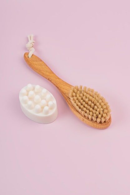 Escova de madeira com cerdas naturais para massagem a seco prevenção de celulite e barra de sabão massageadora em fundo rosa Home SPA minimalismo