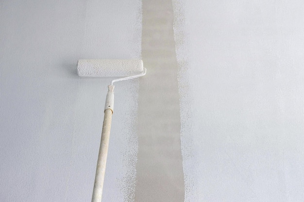 Escova de rolo de cabo longo aplicando tinta branca de primer no fundo da parede de cimento