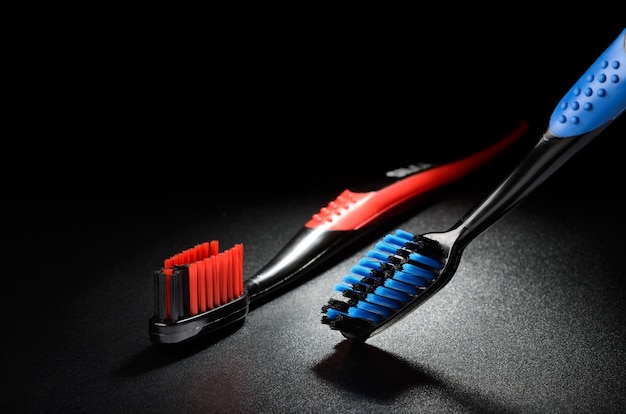 Escovas de dente azuis e vermelhas em uma superfície granulada preta