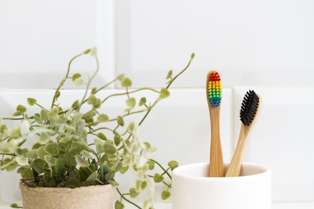 Foto escovas de dente de bambu em um vidro de cerâmica em frente a uma parede de azulejos