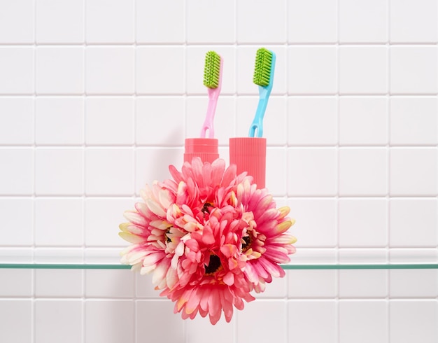 Escovas de dentes coloridas e flores sobre um fundo de azulejos brancos Dentes saudáveis e cuidados