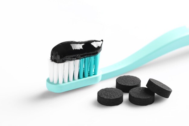 Foto escove com pasta de dente de carvão e pílulas no fundo branco