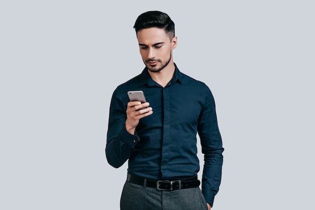 Escribiendo mensaje rápido. Hombre joven serio en camisa escribiendo un mensaje de texto usando su teléfono inteligente