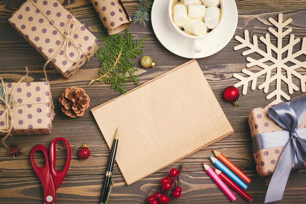 Escribir tarjetas de felicitación de navidad. Bloc de notas abierto con bolígrafo sobre mesa de madera decorada