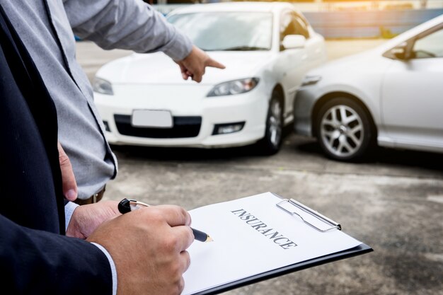 Escrita do agente na prancheta enquanto examina o carro após uma reivindicação de acidente