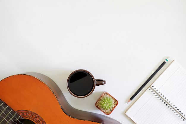 El escritor de canciones presenta un espacio de trabajo con una guitarra acústica y una taza de café con papel de bloc de notas en el escritorio de la vista superior.