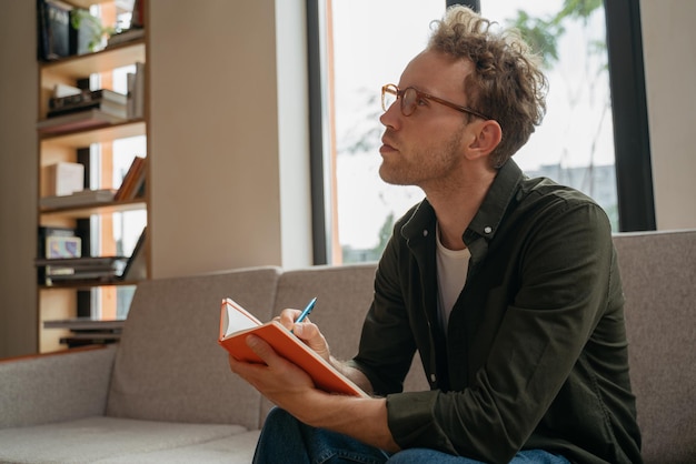 Foto escritor de homem bonito tomando notas no local de trabalho estudante pensativo estudando sentado na biblioteca