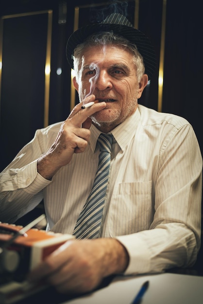 Escritor de homem sênior retrô com chapéu e um cigarro na boca, pensando. Olhando para a câmera.