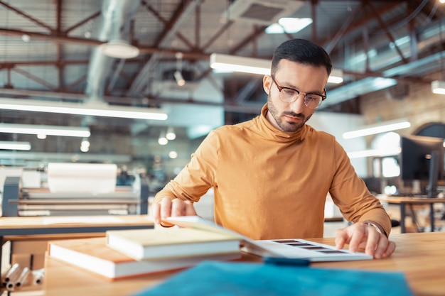 Escritor con gafas. Inteligente escritor famoso de pelo oscuro con gafas eligiendo el color para la portada del libro