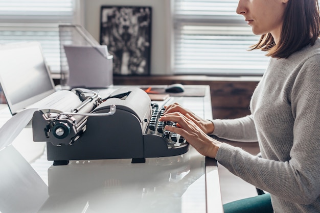 Escritora escribiendo en una máquina de escribir sentada en su sala de trabajo.