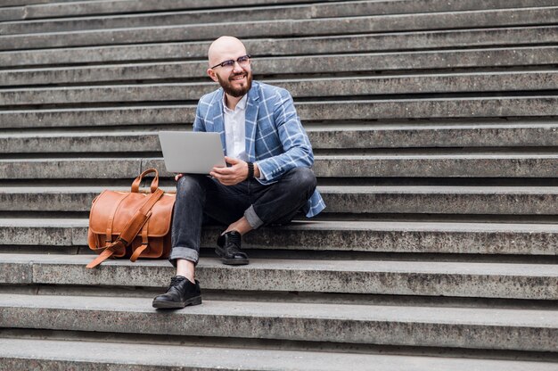 Escritório ao ar livre. Homem moderno em roupa formal e sentado na escada do escritório ao ar livre. Homem usando laptop