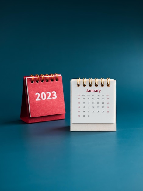 Escritorio de calendario de enero de 2023 para que el organizador planifique y recuerde sobre fondo azul estilo vertical Calendario de mesa blanca con el primer mes cerca de la cubierta roja con números de año 2023 Feliz año nuevo