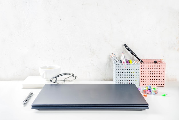 Escritorio creativo de oficina con suministros y taza de café. Mesa de oficina blanca con laptop, teclado, cuaderno en blanco, gafas, suministros y taza de café. Vista superior del espacio de copia de diseño Flatlay