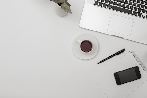 Escritório de mesa com laptop, bloco de notas em branco, xícara de café e caneta na mesa branca. espaço da cópia da vista superior plana leiga.