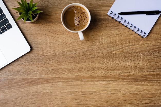 Escritório de mesa com laptop, caderno em branco e xícara de café na mesa de madeira