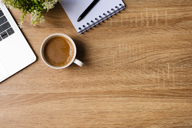 Escritório de mesa com laptop, caderno em branco e xícara de café na mesa de madeira