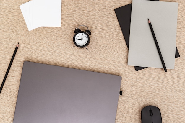 Escritorio para estudiantes o autónomos. Espacio de trabajo. Lugar de trabajo con laptop gris moderna, taza de café, vasos y reloj para controlar el tiempo en la mesa de luz. Endecha plana.