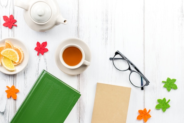 Escritorio femenino espacio de trabajo plano con diario, anteojos, libro, taza de té, dulces y decoración de fieltro.