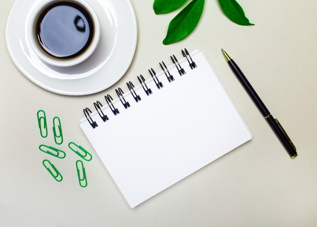 En el escritorio hay una taza blanca con café, una planta verde y sujetapapeles, un bolígrafo y un cuaderno en blanco con un lugar para insertar texto.