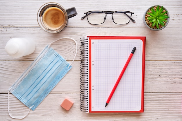 Escritorio con libreta, lápiz, café y máscara. Concepto de protección contra el virus covid.