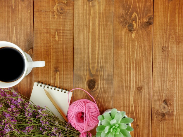 Escritorio de madera marrón, vista superior, plano, con papelería, una taza de café, flores y espacio de copia