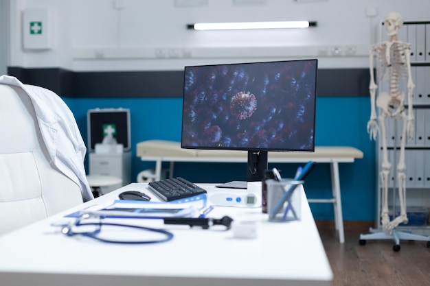 Escritório moderno vazio com computador em pé na mesa da mesa com célula de vírus na tela durante a pandemia global de coronavírus. sala de exames equipada com ferramentas profissionais. conceito de medicina